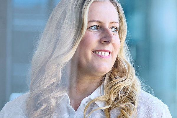 Bild einer jungen Frau mit blondem, gelocktem Haar, die freundlich lächelt