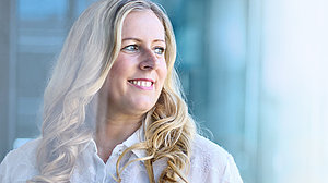 Bild einer jungen Frau mit blondem, gelocktem Haar, die freundlich lächelt