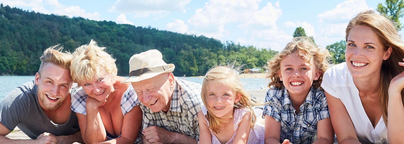 Bild: mehrere Generationen (vom Kind bis zum Opa) liegen glücklich lächelnd auf dem Steg an einem See