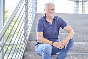 Foto: ein Mann sitzt auf einer Treppe und lächelt freundlich