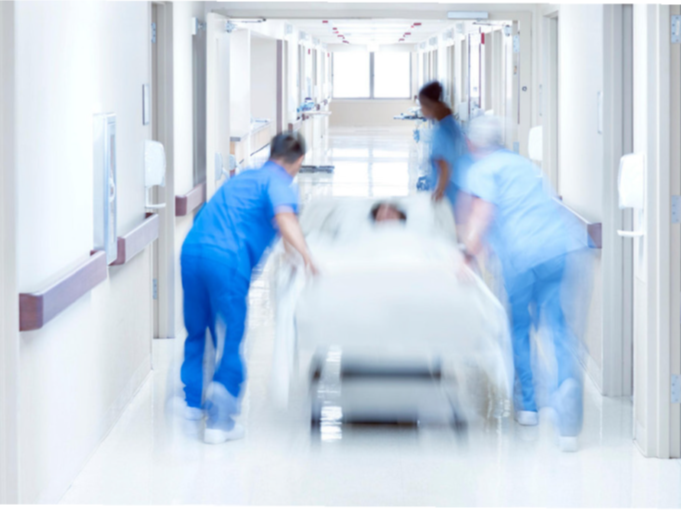 Bild: Drei Menschen in blauer Kleidung schieben einen Patienten &uuml;ber einen Krankenhausflur. Unsch&auml;rfe im Bild soll die Schnelligkeit verdeutlichen.