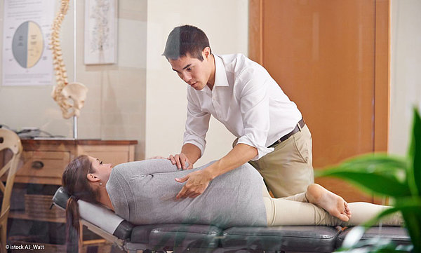 In einer Praxis: Ein Osteopath behandelt eine liegende Frau am R&uuml;cken.